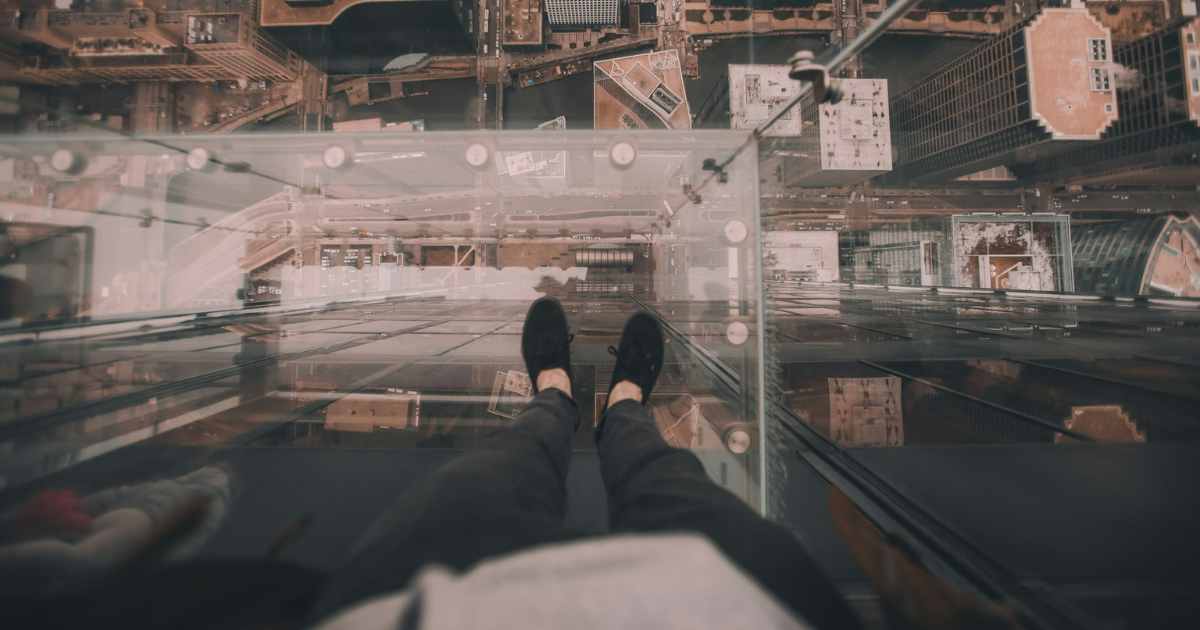 A person standing on a see-through platform high above buildings represents the fear that's behind the costliest organizational tradeoffs.