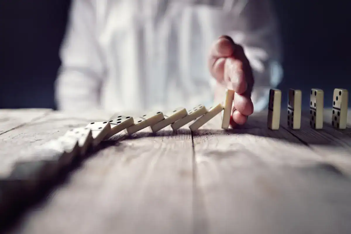 A man stopping a line of dominoes from falling in line, disrupting the pattern like many organizations do with their strategy.